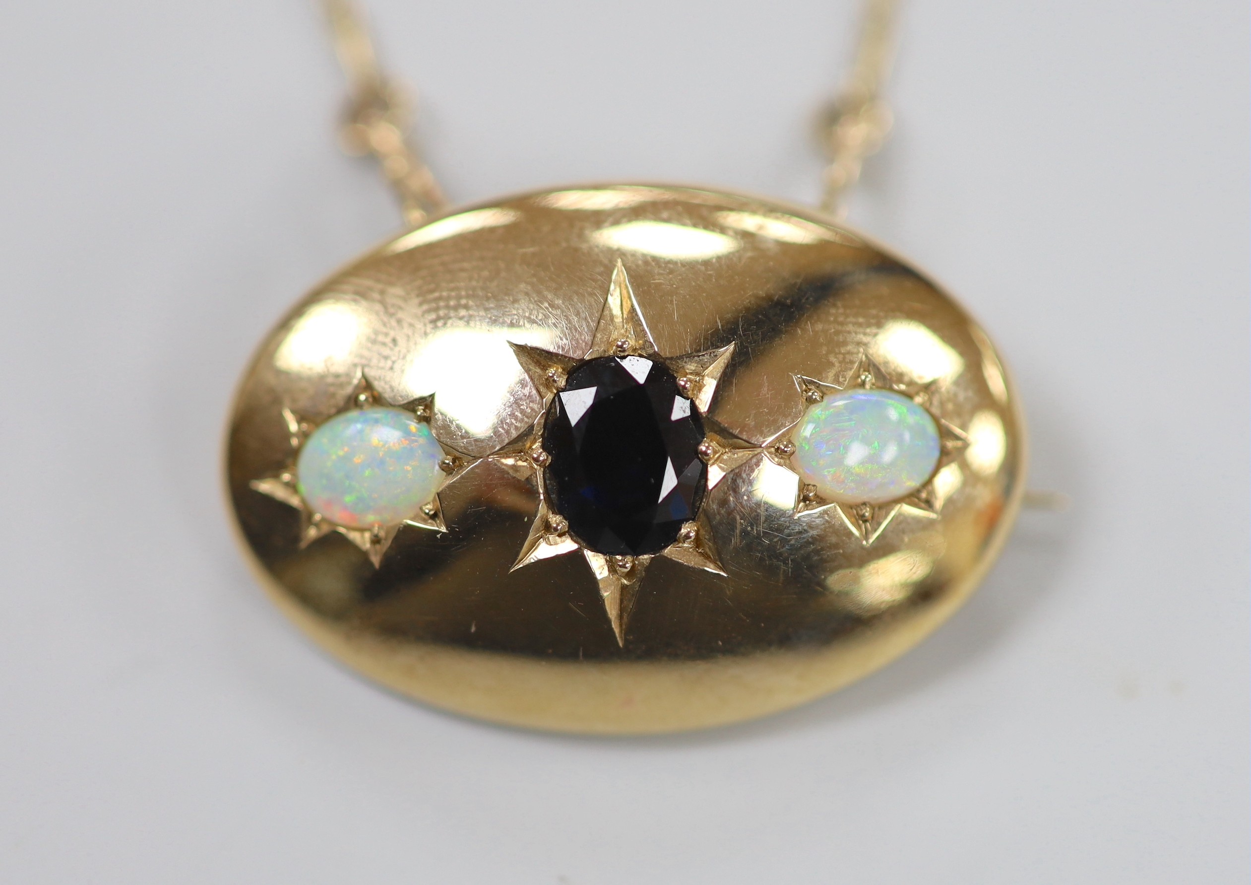 A 1970's 9ct gold and gypsy set single stone sapphire and two stone white opal set oval pendant brooch, 34mm, on a 9ct gold chain, 46cm, gross weight 15.9 grams.